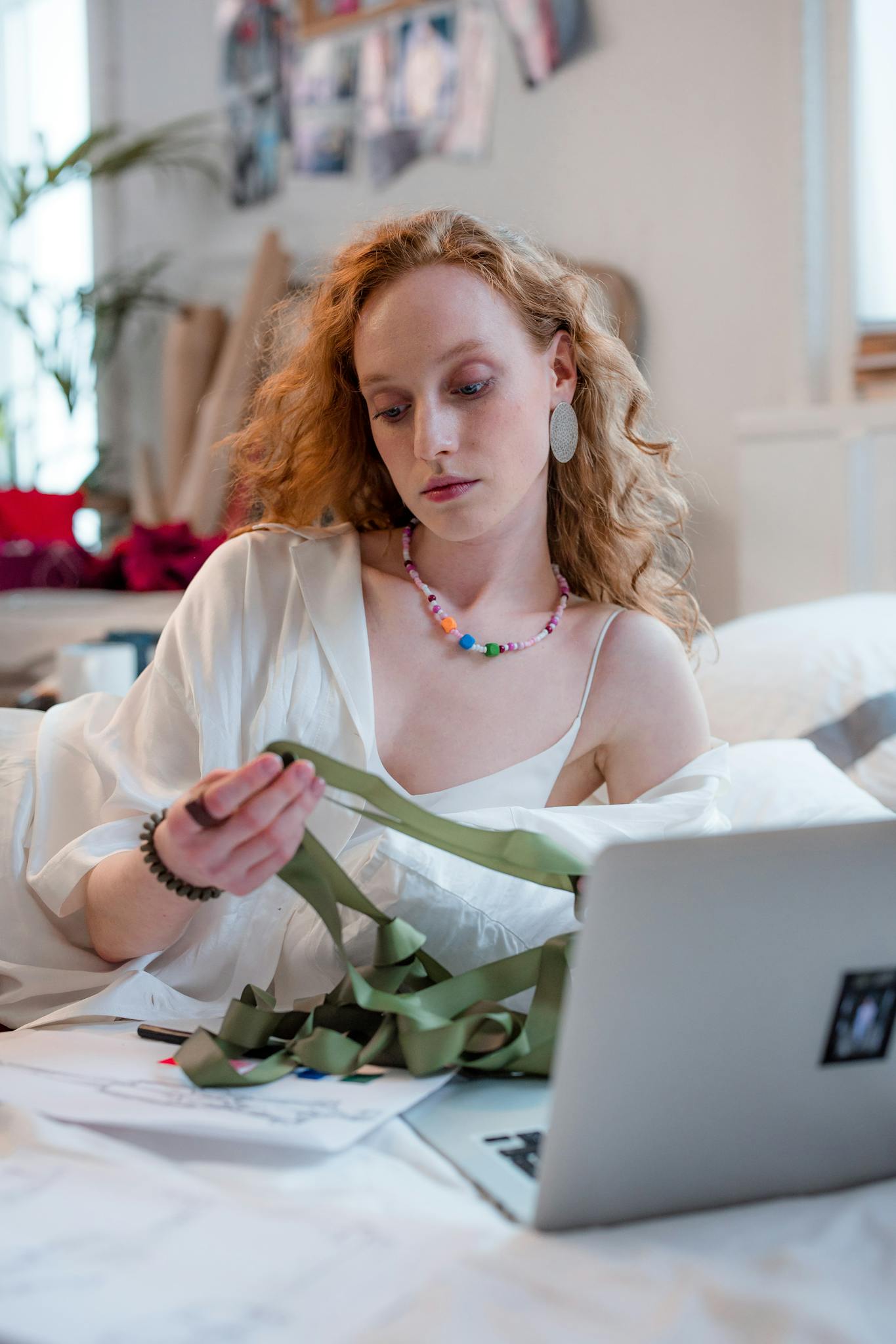 A focused woman in a cozy home setting working with ribbon and laptop, showcasing creativity and concentration.